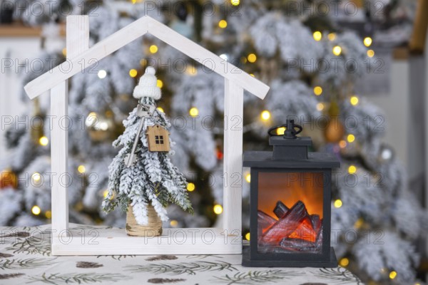 Key on Christmas tree and tiny house on cozy home with Christmas decor on table of festive white kitchen. Gift for New Year. Insurance, moving to new house, mortgage, rent and real estate