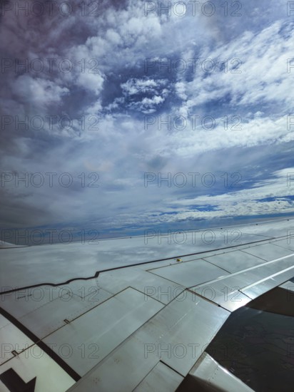 Aircraft wings under a wide sky with dramatic cloud formations, the return flight from holiday