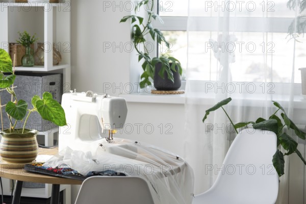 Sewing machine on a round table in the white interior of the house near the window with a transparent curtain, and a home plant in a pot, a modern interior. hobby, home business