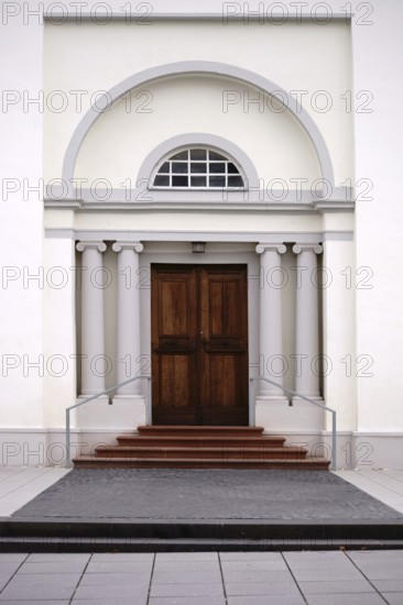 The entrance of a newly built and modern church with an entrance door with a round arch and white walls