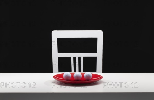 Three white golf balls on the red plate. White old chair and white table in the dark room