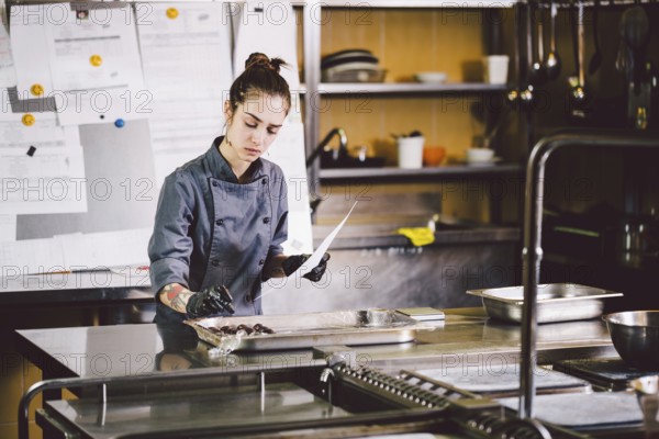 Subject profession and cooking pastry. young Caucasian woman with tattoo of pastry chef in kitchen of restaurant preparing round chocolate candies handmade truffle in black gloves and uniform