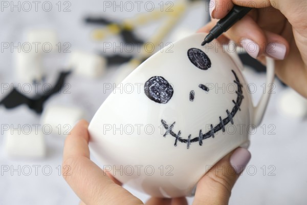 Female hands paint on white cup scary jacks face DIY for kids Halloween home activities Holiday art children craft Handmade decorations. Step by step Socially distanced at home Idea for art class