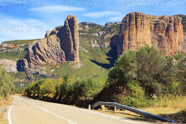 Asphalt highway passes through the rocks. Part of the foothills of the Pyrenees. The Mallets of Riglos. Hot sunny afternoon. Romantic trip to Spain. Hoya de Huesca, Aragon
