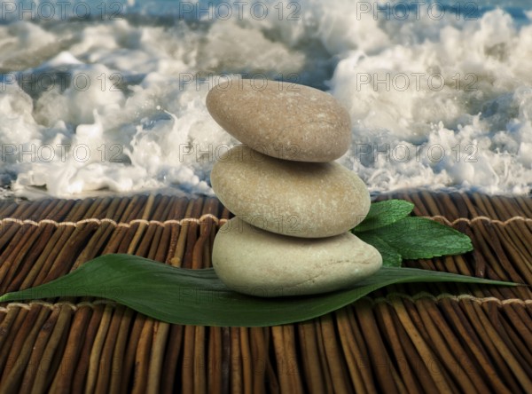 Stacked stones on wooden base for spa and green leafs. Waves on the background