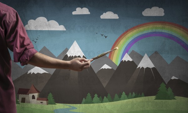 Close up artist hand holding paintbrush. Painter in shirt standing on background colorful picture. Summer landscape with mountains, blue sky and rainbow artwork. Creative hobby and profession