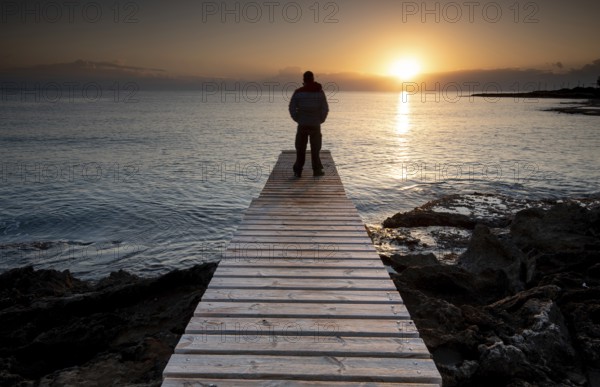 Person standing at the edge of a wooden pier in the sea at sunrise, People active outdoors enjoy ocean. Protaras Cyprus