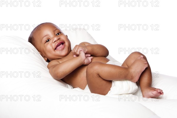 Happy cute smiling laughing African baby infant laying wearing diapers on soft bed, isolated, Atlanta, USA