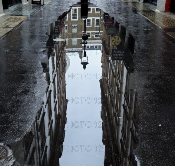 Street scene with puddle reflecting brick buildings and lanterns creates urban and wet ambience, Covent Garden London WC2E 8RA, England, United Kingdom