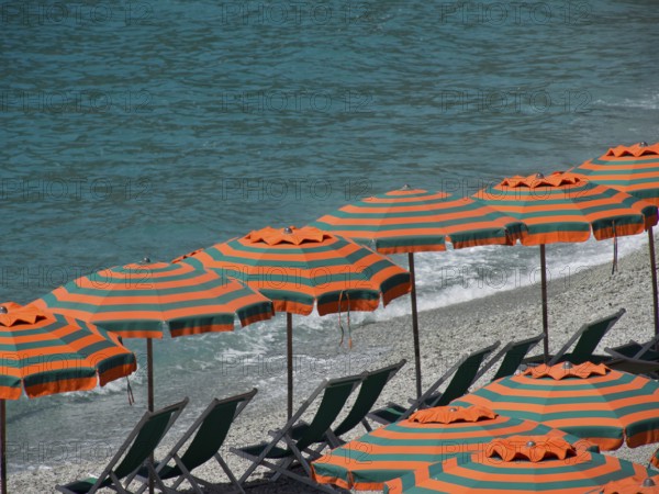 Row of striped parasols on a pebbly beach with a view of the sea and gentle waves, Monte rosso, cinque terre, Italy