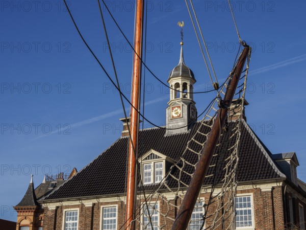 Building with clock tower and sailing mast in the foreground under a blue sky, empty, East Frisia, Germany