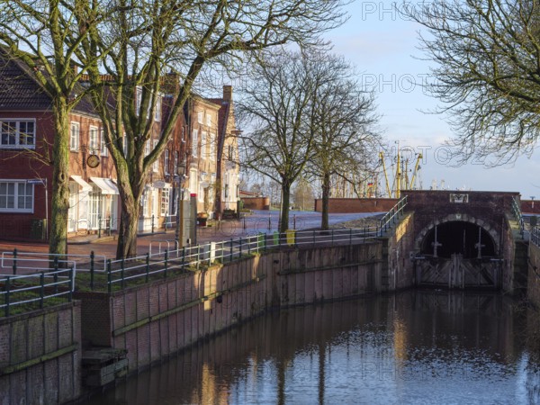 Urban scene with canal lined with trees and buildings. Bridge and reflection visible in the water, Greetsiel, East Frisia, Germany