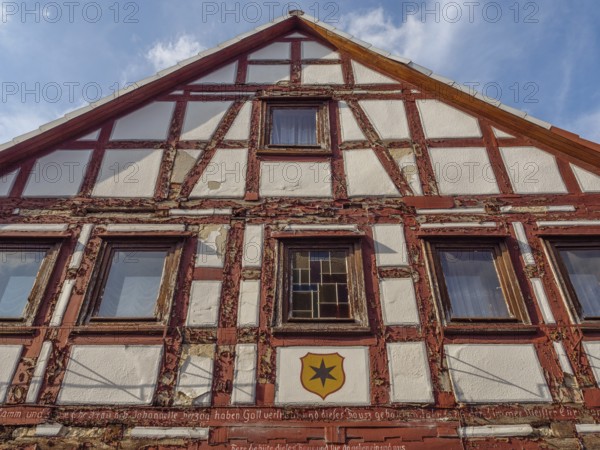 Historic half-timbered facade of a house with coat of arms under blue sky and clouds, waldeck, hesse, germany