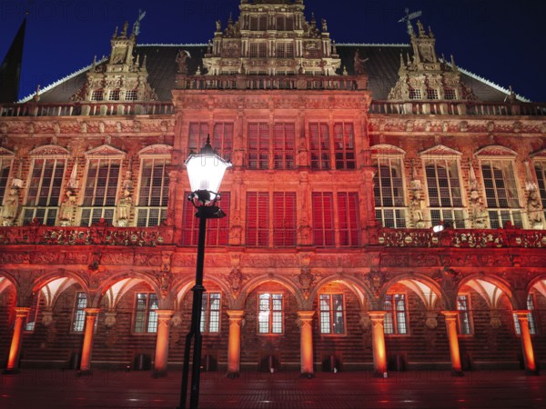 Impressive gothic building with red lighting and a lantern in the foreground at night, Bremen, Germany
