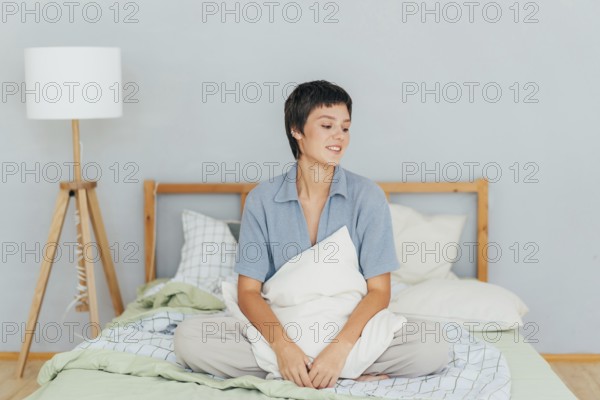 Junge kaukasische Brünette sitzt auf dem Bett in der Wohnung