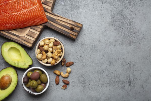 Food sources of healthy unsaturated fat and omega 3: fresh raw salmon fillet, avocado, olives, nuts on cutting board, rustic stone background top view. Healthy nutrition and keto diet, space for text, food photography, food photography