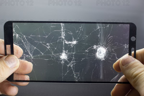Broken protective glass of smartphone with cracks in hands on black background. Damaged protective glass, photo while replacing screen protector, cellphone repair