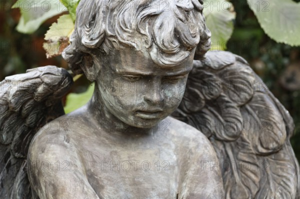 Little angel in a cemetery looks sadly to the ground