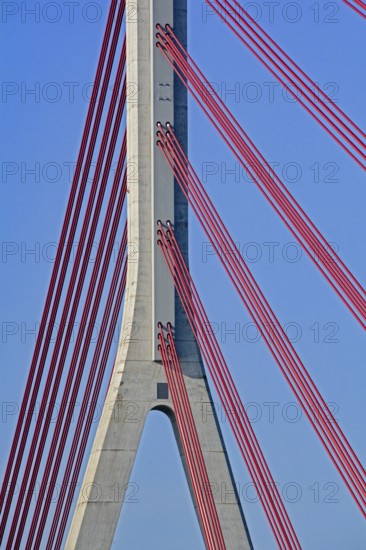 Close-up of red cables supporting a concrete pillar of a modern cable-stayed bridge against a vibrant blue sky