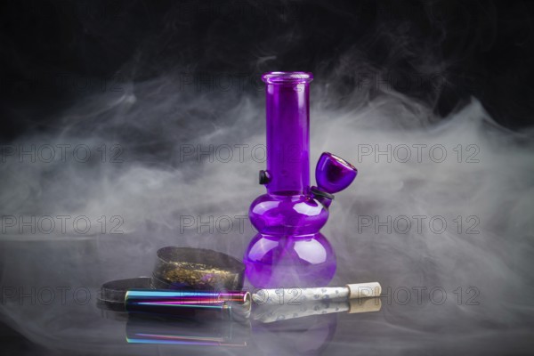 Purple glass bong pipe with joint and a lot of smoke. Cannabis smoker starter pack