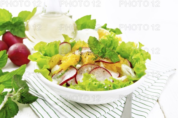 Radish, onion and orange salad with mint, vegetable oil and spices on lettuce in a plate on a towel on white wooden board backgroun