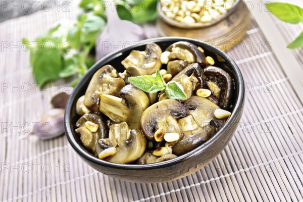 Champignons baked with oregano, wine, garlic, lemon and pine nuts in bowl on background of brown bamboo napkin
