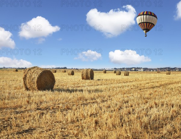 Red and blue balloon slowly floating over kibbutz field. Stacks of harvested wheat beautifully and symmetrically stand in rows