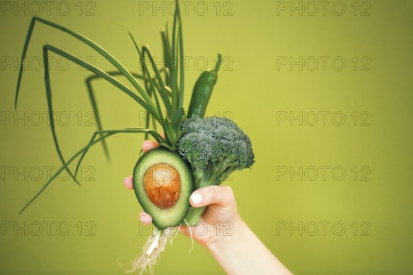 Unrecognizable female demonstrating bunch of healthy fresh vegetables while being on diet against green background