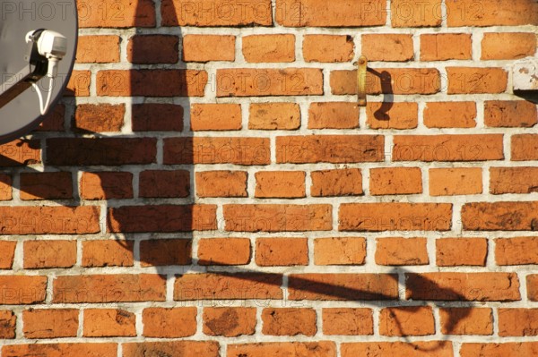 A satellite dish on a brick building casts a shadow