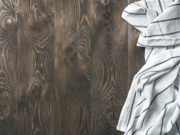 View from above on brown wooden table with linen kitchen towel or textile napkin. Blue tablecloth on dark brown wood tabletop. Copy space for text. Can use as mock up for design