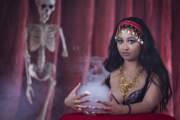 A fortune teller with an oriental look next to a skeleton and a fog vessel, studio shot, staged photo shoot, Mindelheim, Unterallgäu, Bavaria, Germany