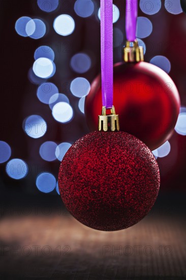 Two red christmas balls hanging on pink tape on old wooden table and blurred bokeh background