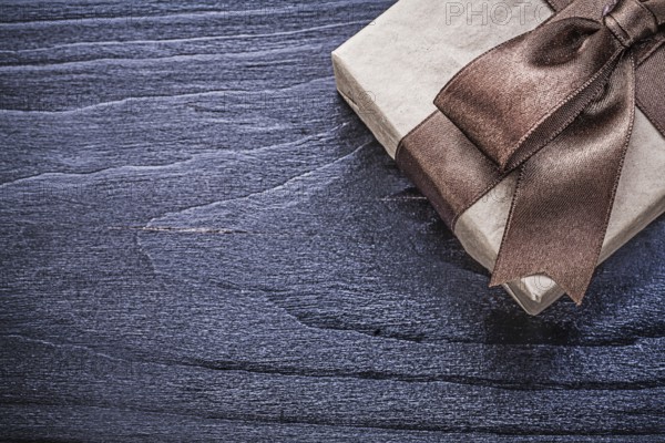 Gift box with brown satin bow on wooden board