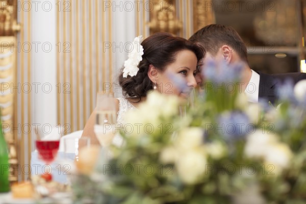 Bride and groom sharing a special tender moment at the wedding leaning with their heads close together as they share their love, view across a bowl of flowers