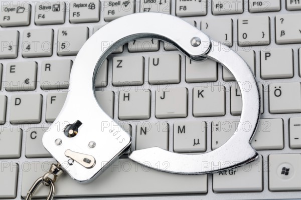 Handcuffs lying on the keyboard of a computer. Symbolic photo for criminality, computer crime and data misuse