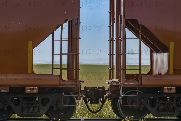 Close up of train coupler connecting two red wagons of a Canadian freight or cargo train. Green fields and blue sky in the background