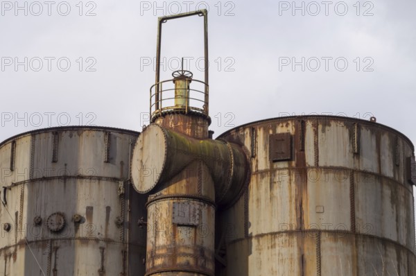 Large rusty industrial tanks and pipes dominate the scene, hinting at a past era of manufacturing and industry