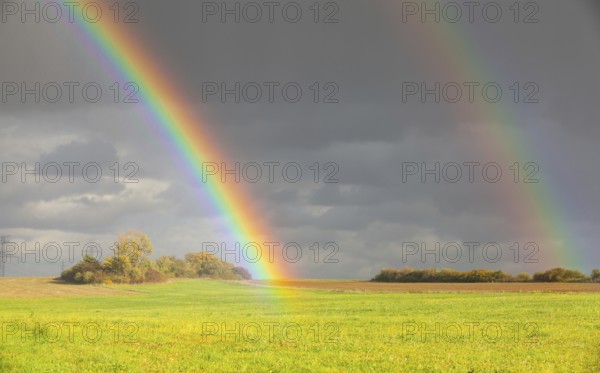 Two natural rainbow over green field after heavy rain