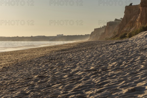 Incredible rock formations by the sea. Red cliffs with red earth and breathtaking formations on the wide sandy beach. Praia da Falésia, bathed in warm light by the sun at sunset, Algarve, Portugal
