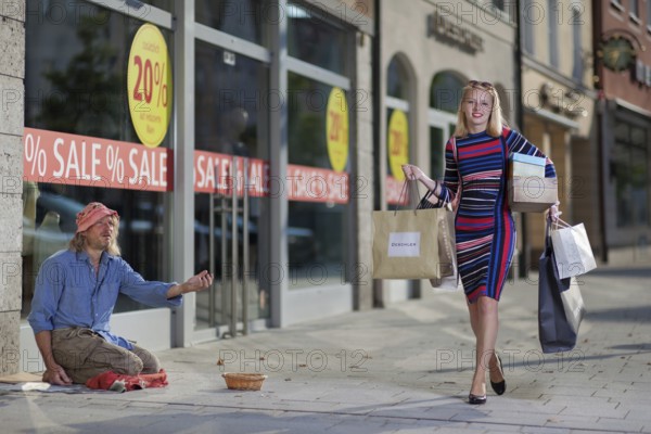 Woman with shopping bags walks past a homeless man on the street, Staged photo shoot, Mindelheim, Unterallgäu, Bavaria, Germany