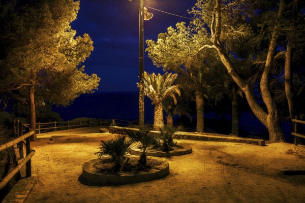 Gloomy square in abandonded park by the sea at midnight illuminated by single lamp, Costa Brava in Lloret de Mar, Catalonia, Spain