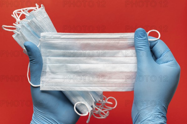 Doctor holds lot respiratory surgical face mask in hands blue medical gloves on red background. Pandemic insurance, coronavirus, airborne diseases, SARS, grippe. Medical human masks cover mouth, nose