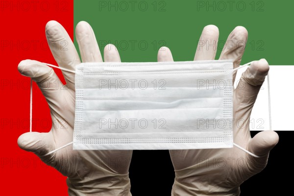 Medic holds protective respiratory face mask in two hands in white gloves on background of national flag of United Arab Emirates UAE. Concept coronavirus quarantine, grippe and pandemic outbreak, flu