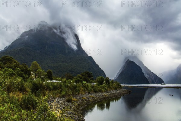 Magic country of fantastic heroes. New Zealand. Storm clouds cover the sky over the famous ocean fjord Milford Sound. Sunlight breaks through storm clouds. Concept of exotic, ecological and photographic tourism
