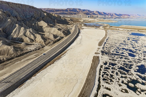 Asphalt highway runs along the sea coast. The picturesque Dead Sea is covered with patterns of salt. The picture was taken by a drone from a aerial view. Israel. Winter sunny day