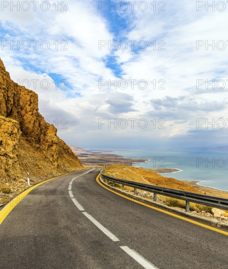 The highway runs along the coast of the Dead Sea. Wonder of nature - the Dead Sea. Cloudy and warm January day. The sea surface reflects the clouds. Israeli coast