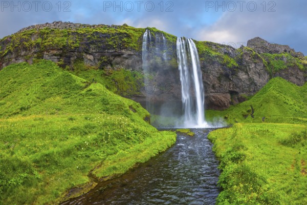 The warm July day in Iceland. Seljalandsfoss waterfall. Rainbow decorates drop of water