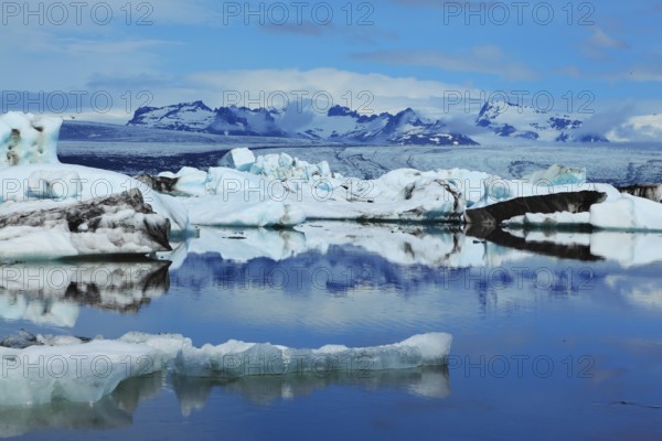Sunrise. Blue and emerald icebergs and ice floes are reflected in smooth water of the Gulf Jökulsárlón in Iceland