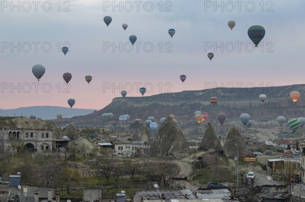 A picture of hot air balloons flying over the Goreme Historical National Park and the town of Goreme at sunrise