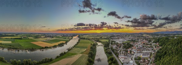 The sunset bathes the landscape in warm light, while the Danube flows calmly and the town of Bogen (Lower Bavaria) is visible in the background. Green fields and rolling hills complete the panorama